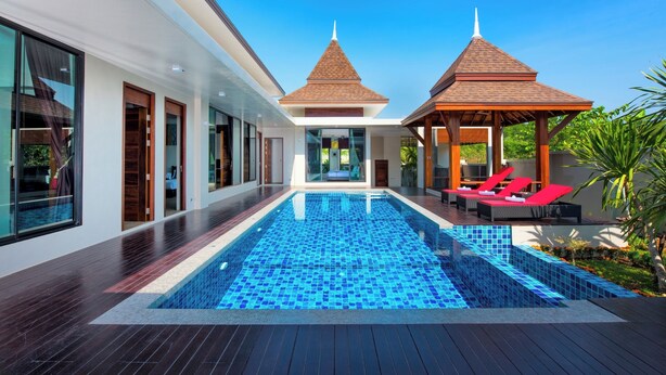 A modern pool area with a clear blue pool, wooden deck, and two gazebos with red lounge chairs.