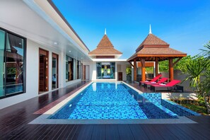 Ein moderner Poolbereich mit klarem, blauem Pool, Holzdeck und zwei Pavillons mit roten Liegestühlen.