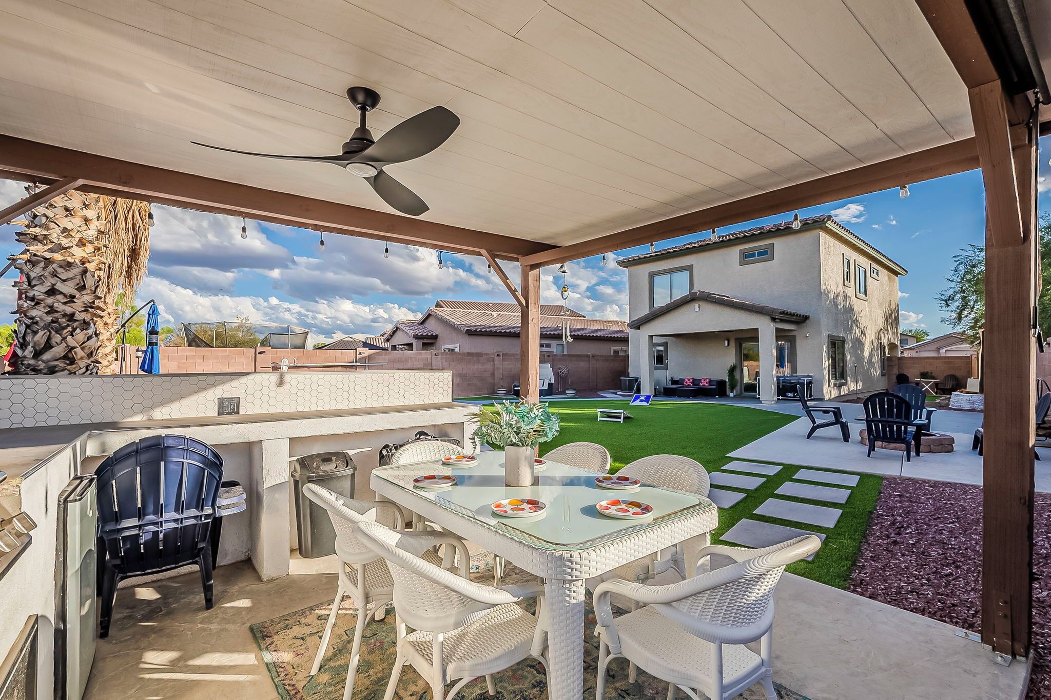 An outdoor patio with a table and chairs, a ceiling fan, and a view of a house in the background.