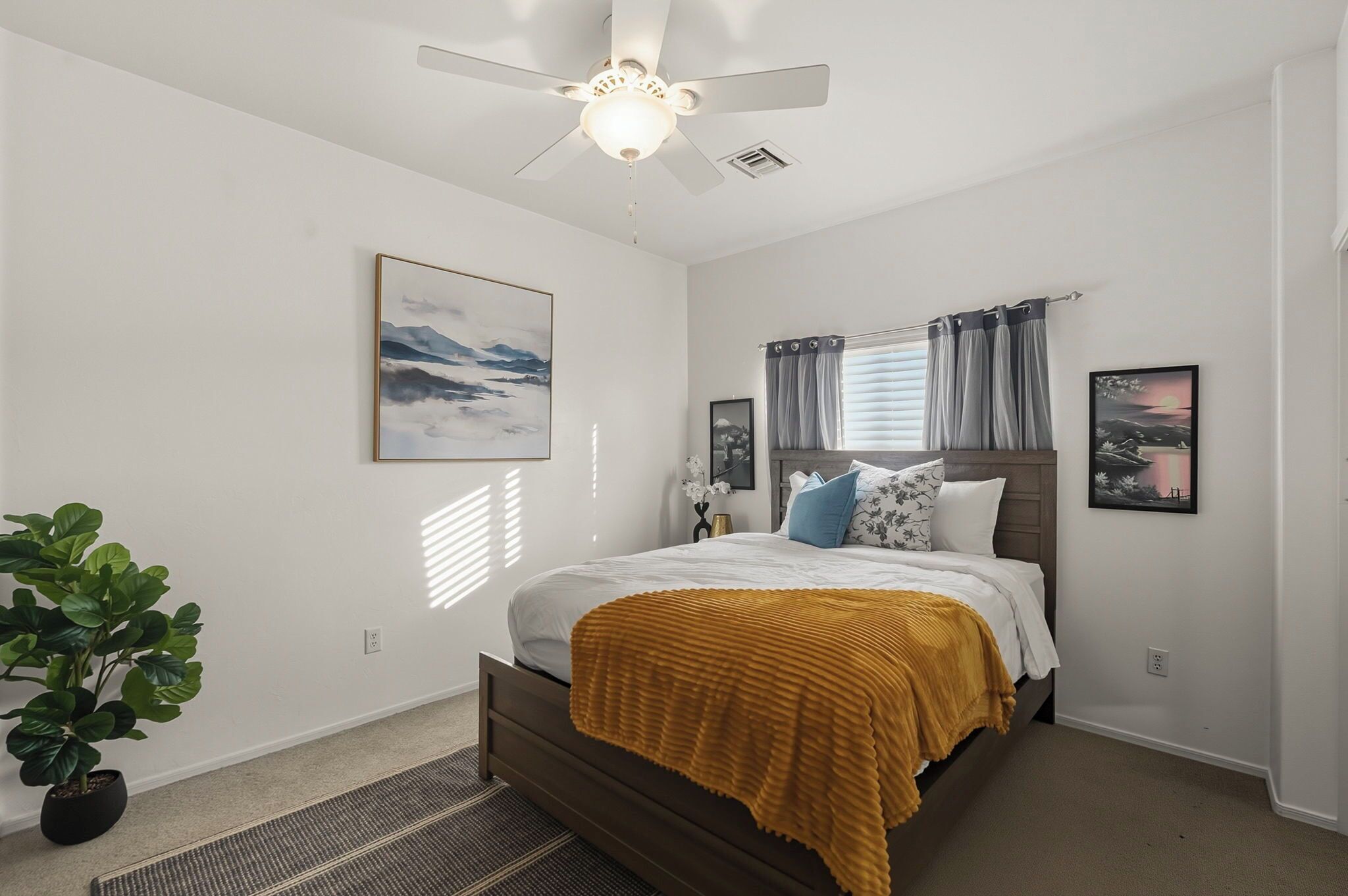 A bedroom with a bed, a ceiling fan, a window with curtains, and a potted plant.