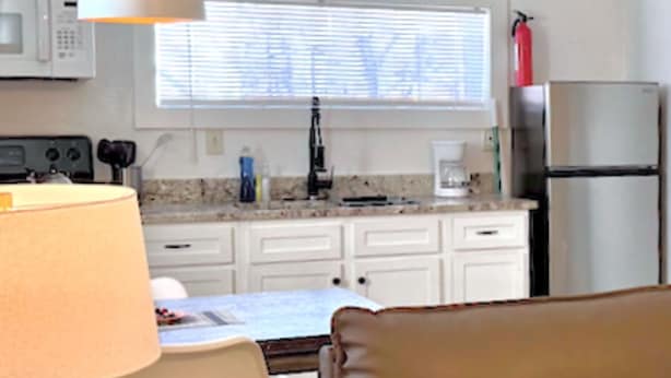 A kitchen with white cabinets, a microwave, a stove, a coffee maker, and a refrigerator. - Fully-furnished Studio With Rustic Design 36B (Oklahoma City)