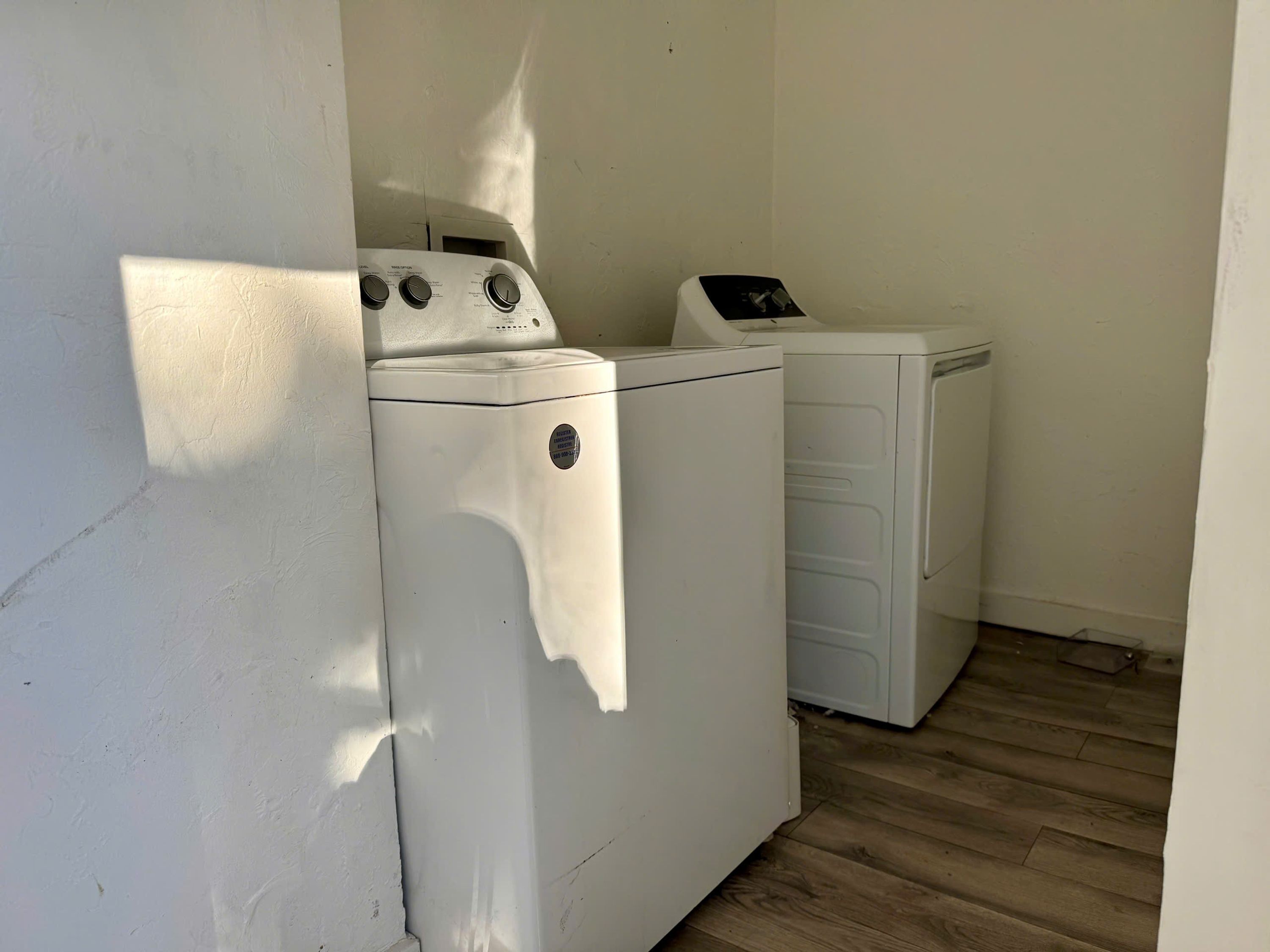 Un lavadero con lavadora y secadora de carga frontal, suelo de madera y pared blanca.