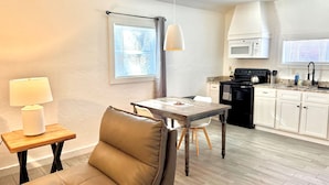 A compact kitchen with a dining area, including a table, chairs, and a lamp. - Fully-furnished Studio With Rustic Design 36B (Oklahoma City)