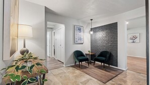 A modern hallway with a wooden floor, two green armchairs, a small table with a plant, and a wall-mounted lamp. - Spacious 8BR Modern Retreat Pool Table RV (Bethany)