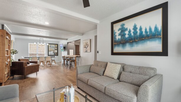 A living room with a grey sofa, wooden cabinet, and a painting of a forest on the wall. - Spacious 8BR Modern Retreat Pool Table RV (Bethany)