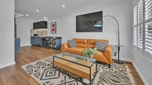 A modern living room with a sofa, coffee table, and a floor lamp. There is a kitchen in the background with a dining area. - The Mac Orange (Orange)
