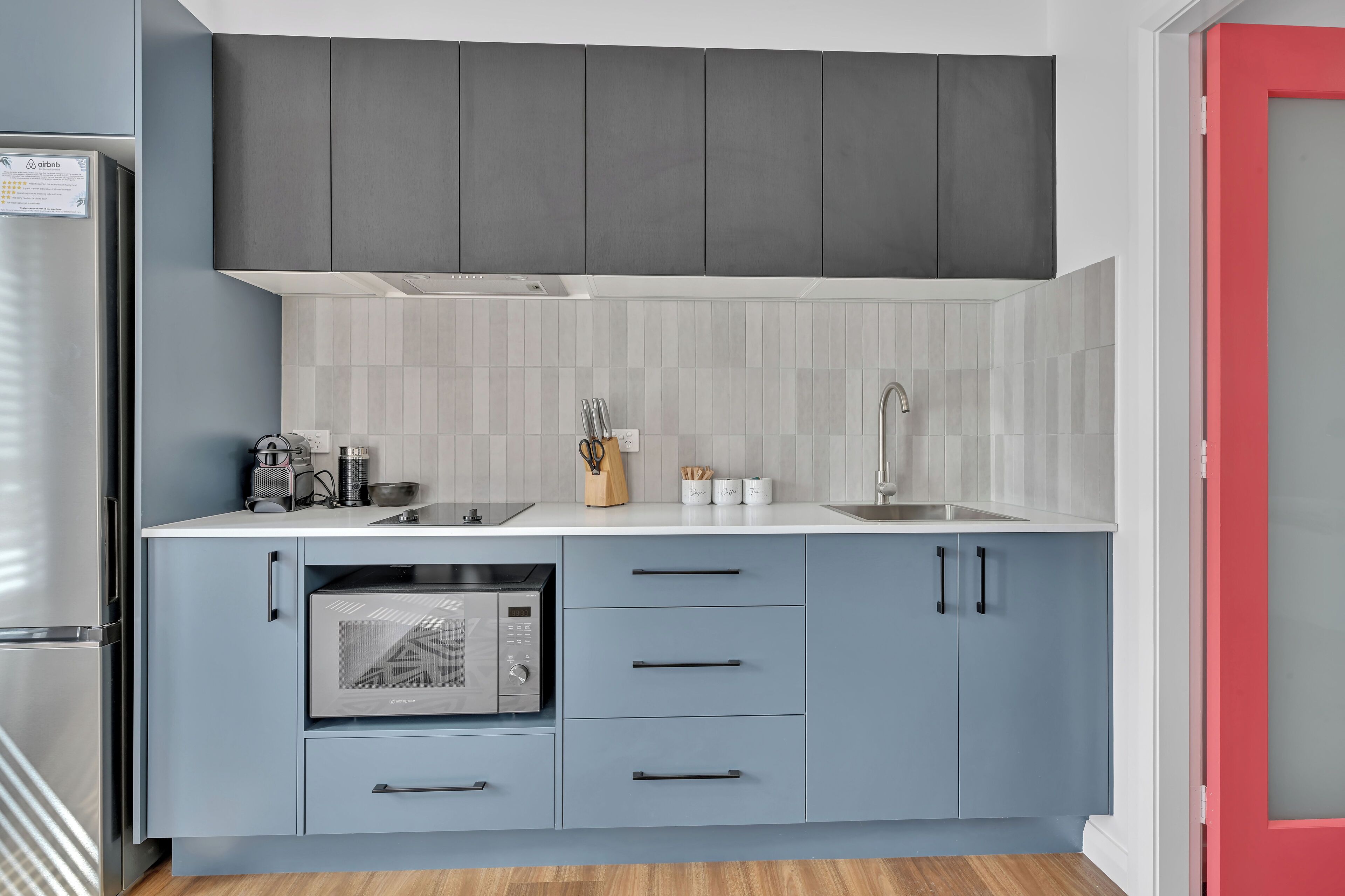A modern kitchen with grey cabinets, a white countertop, and a built-in microwave.