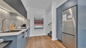A modern kitchen with grey cabinets, a stainless steel refrigerator, and a wooden floor. - The Mac Orange (Orange)