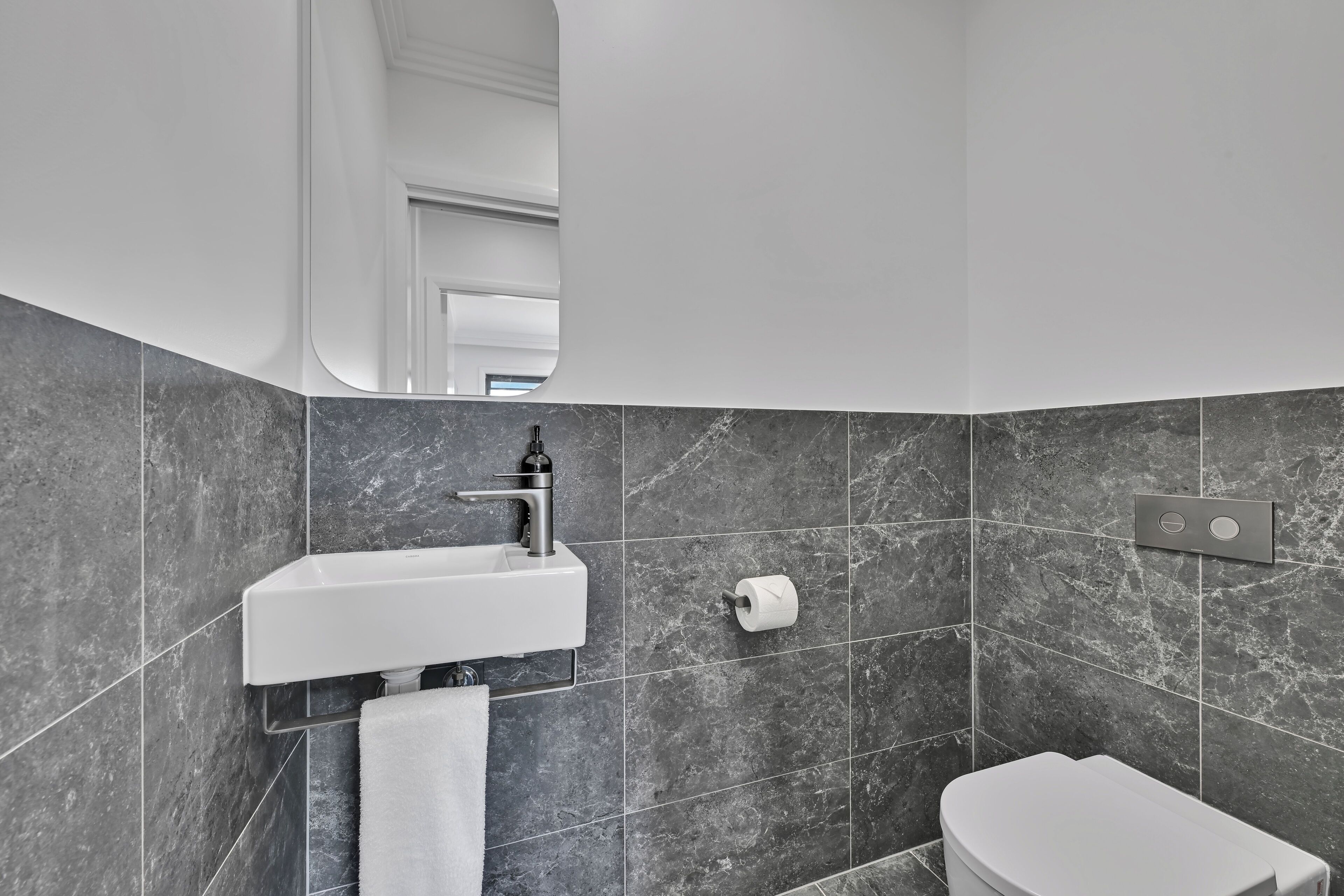Un bagno moderno con un lavandino bianco, piastrelle in marmo, un WC e uno specchio.