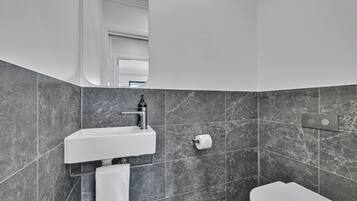 Un bagno moderno con un lavandino bianco, piastrelle in marmo, un WC e uno specchio.