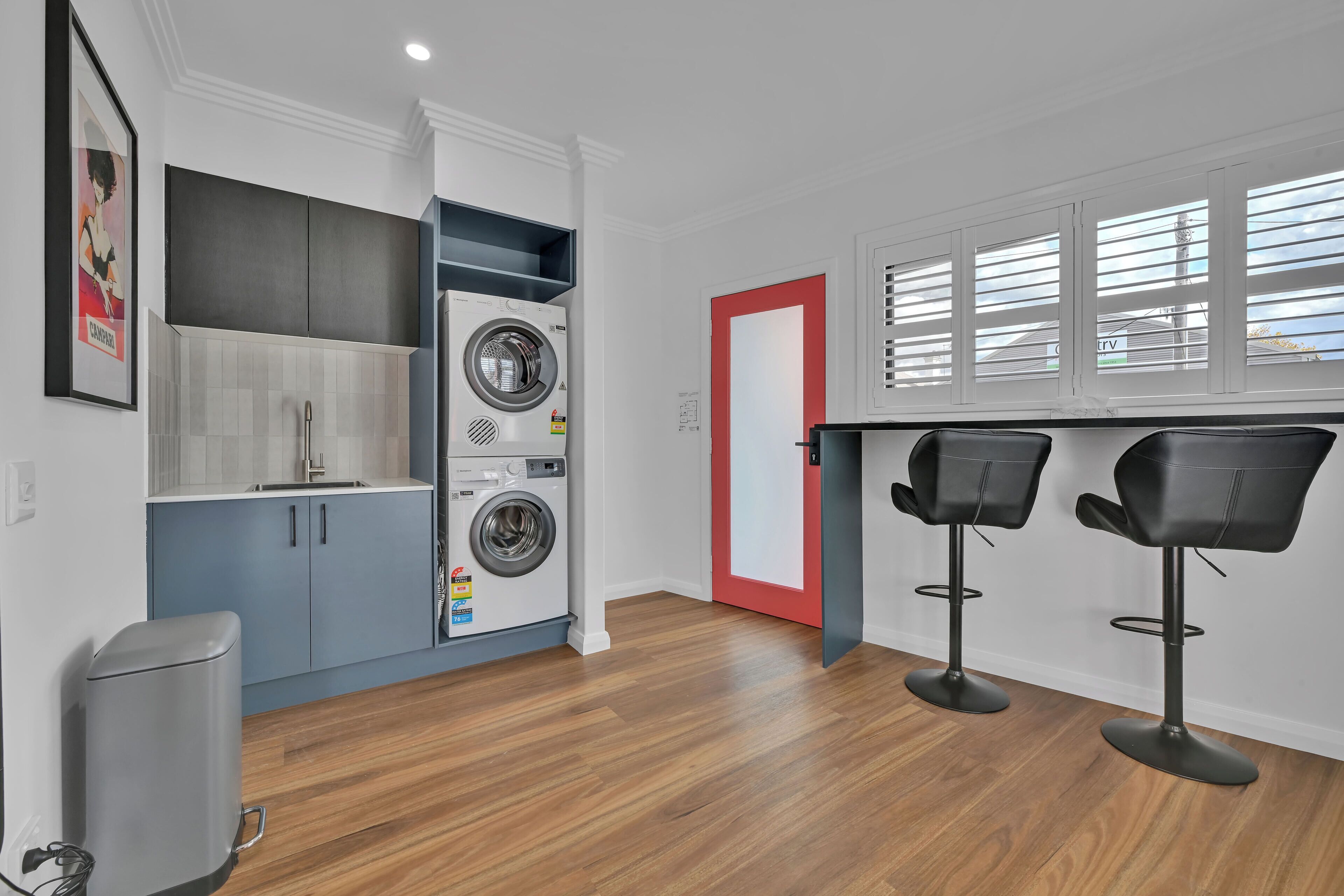 Une cuisine compacte dotée d’un lave-linge et d’un sèche-linge intégrés, d’un petit coin bar avec deux tabourets et d’une porte à cadre rouge.