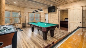Een kamer met houten vloer, een pooltafel, een tafelvoetbalspel en een biljarttafel.