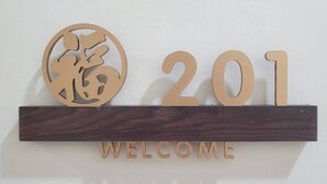 Ein hölzernes Willkommensschild mit den Zahlen „201“ und dem Wort „WELCOME“ auf einem dunklen Holzbrett.