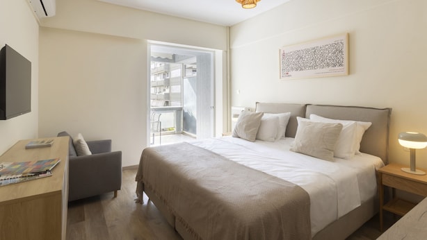 A bedroom with a bed, bedside table, lamp, and a view of an outdoor balcony. - Thiseos 5-7·Renovated Studio with Sea View (Palaio Faliro)