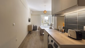 A modern kitchen with a built-in washing machine, a toaster, and a window providing natural light. - Thiseos 5-7·Renovated Studio with Sea View (Palaio Faliro)