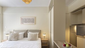 A neatly arranged hotel room with a bed, bedside table, lamp, and a small dining table with apples. - Thiseos 5-7·Renovated Studio with Sea View (Palaio Faliro)
