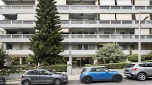 A multi-story residential building with balconies, parked cars, and a tall evergreen tree in front. - Thiseos 5-7·Renovated Studio with Sea View (Palaio Faliro)