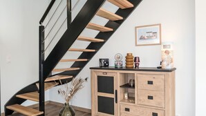 Eine moderne Treppe mit Holzboden und schwarzen Geländern, eine Holzkabine mit Schubladen und eine Vase mit Trockenpflanzen.