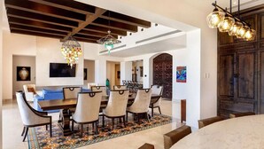 Un vaste espace dédié à la salle à manger, avec une grande table et des chaises en bois, un tapis à motifs et un lustre moderne.