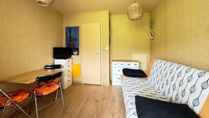 A compact room with a wooden desk, a sofa with patterned cushions, a television on a cabinet, and two wicker pendant lights. - Appt Confortable in Superdévoluy (Le Dévoluy)