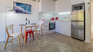 Cocina compacta con armarios blancos, microondas, refrigerador, horno pequeño y un comedor con mesa y sillas.