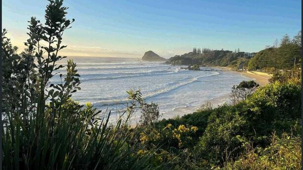 Paisaje costero con playa, olas del océano y una montaña distante.