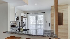 A modern kitchen with granite countertops, stainless steel appliances, and wooden stools. - Beautiful condo in central Scottsdale (Scottsdale)