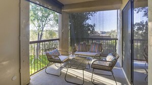 A covered balcony with wicker furniture, a glass door, and a view of trees and a building. - Beautiful condo in central Scottsdale (Scottsdale)