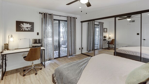 A modern bedroom with a large bed, a desk with a chair, a ceiling fan, and a sliding glass door leading to a balcony. - Beautiful condo in central Scottsdale (Scottsdale)