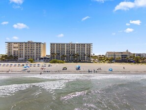 Ein Strandhotel mit mehreren Etagen, einem Sandstrand und Sonnenschirmen.