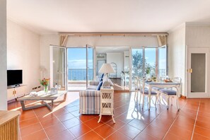 Un amplio salón con sofá, mesa de comedor y sillas, televisor y balcón con vistas.