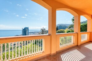 Un balcón con vistas al mar y al paisaje urbano, que presenta suelo de baldosas y balaustradas blancas.