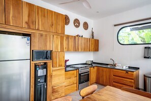 Enjoy cooking in this kitchen with a refrigerator, water dispenser, microwave, and stove, plus a window with a view of lush greenery.