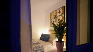 Een slaapkamer met een bed, kussens, een plant en een schilderij aan de muur.
