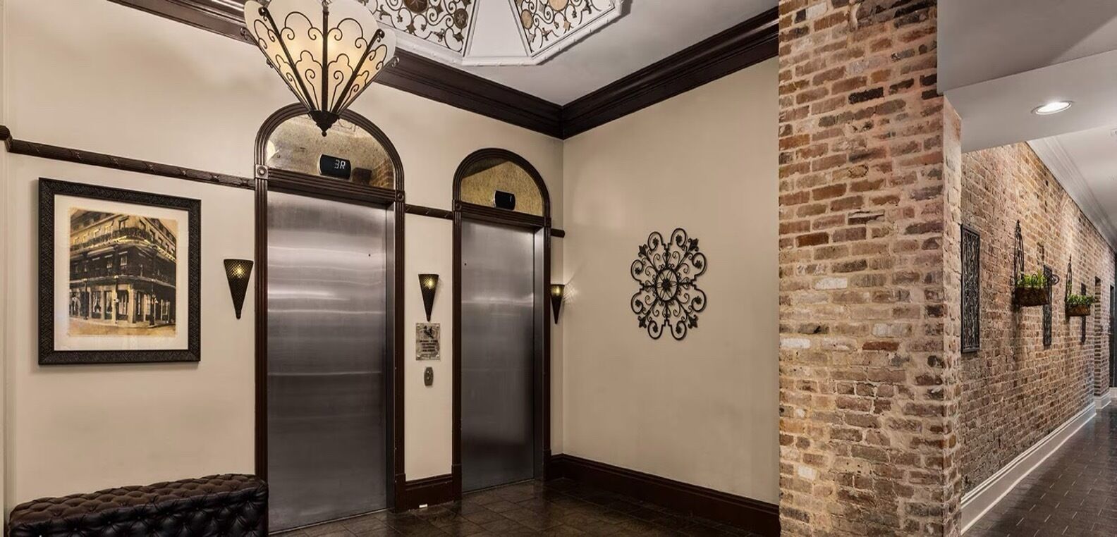 A hallway with two elevators, a framed historical photo, a decorative wall piece, and a brick wall.