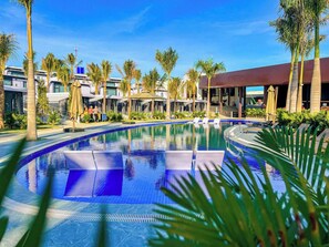 A swimming pool with lounge chairs, palm trees, and a covered area with umbrellas. - Olee Sea View Resort (Mui Ne)