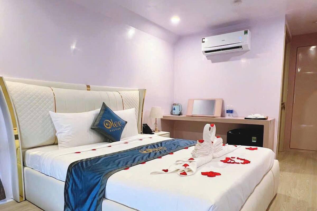 Quarto de hotel com uma cama grande, mesa de cabeceira, aparelho de ar condicionado e piso de madeira.