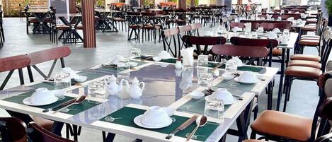 A spacious outdoor dining area with multiple tables and chairs, large pillars, and a covered ceiling.