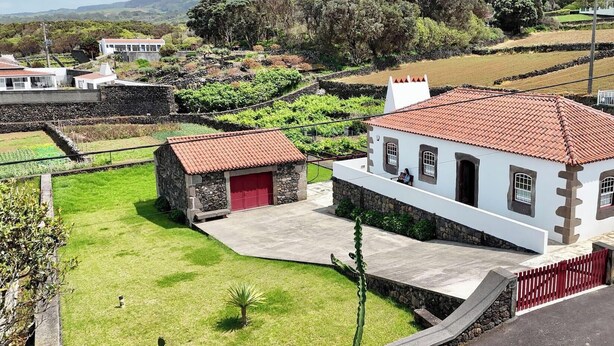 Un edificio blanco con techo rojo, una estructura de piedra con puerta roja y un área verde con un cactus.