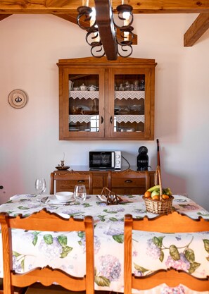 A dining area with a table set for two, a microwave, a coffee maker, and a cabinet with glass doors.
