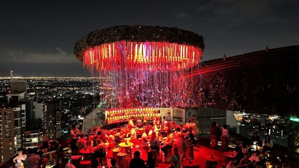 Un bar en la azotea con una zona de estar circular y una gran estructura iluminada arriba.