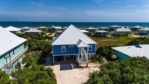 A coastal residential area with multiple houses, a clear view of the ocean, and a sandy path leading to a house with a porch. - Fish N' Fins | Fort Morgan Cabana Beach 180° Gulf Views | Rooftop Terrace | Wraparound Deck (Gulf Shores)
