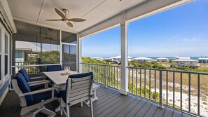 Ein überdachter Außenbereich mit Tisch und Stühlen, einem Deckenventilator und Blick auf Strand und Meer.