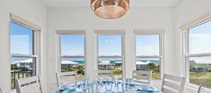 Ein Essbereich mit einem Tisch für vier Personen, großen Fenstern mit Blick auf den Strand und einer hängenden Leuchte.