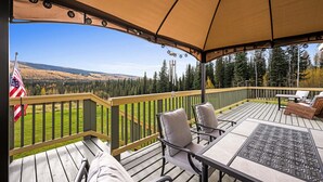 A covered deck with outdoor seating and a view of a forested landscape. - Aurora Panorama Lodge- Perfect Retreat 5b3b (Fairbanks)