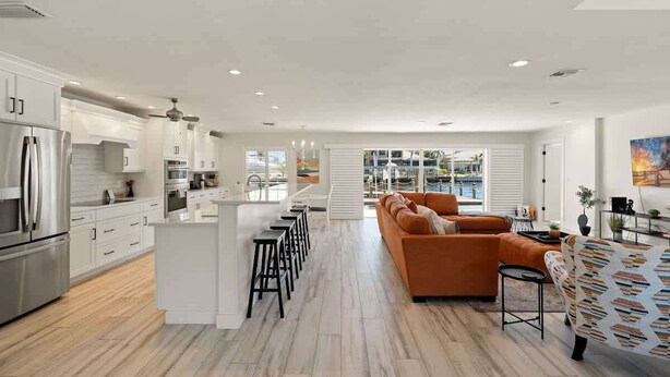Une cuisine moderne avec des meubles blancs, un îlot central doté de tabourets et un coin repas avec des meubles orange.