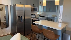 A modern kitchen with stainless steel appliances, a marble countertop, and pendant lighting. - Oceanfront Hideaway with Detached Primary Bedroom (Ewa Beach)