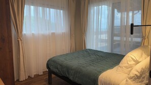 A bedroom with a bed, wooden floor, and sheer curtains. - Oceanfront Hideaway with Detached Primary Bedroom (Ewa Beach)