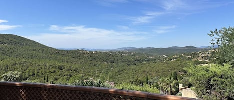 A terrace with a view of a hilly landscape, a lattice fence, and a table.