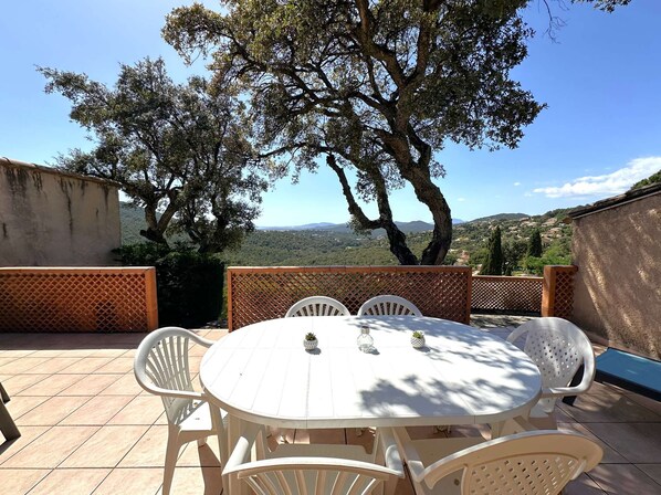 An outdoor patio with a round table and chairs, surrounded by a wooden fence, overlooking a scenic landscape.
